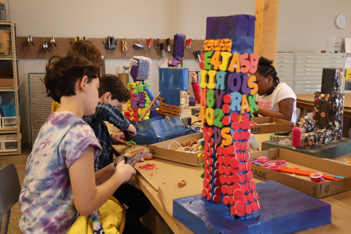 Kids sitting at a table work on sculptures made of mixed materials
