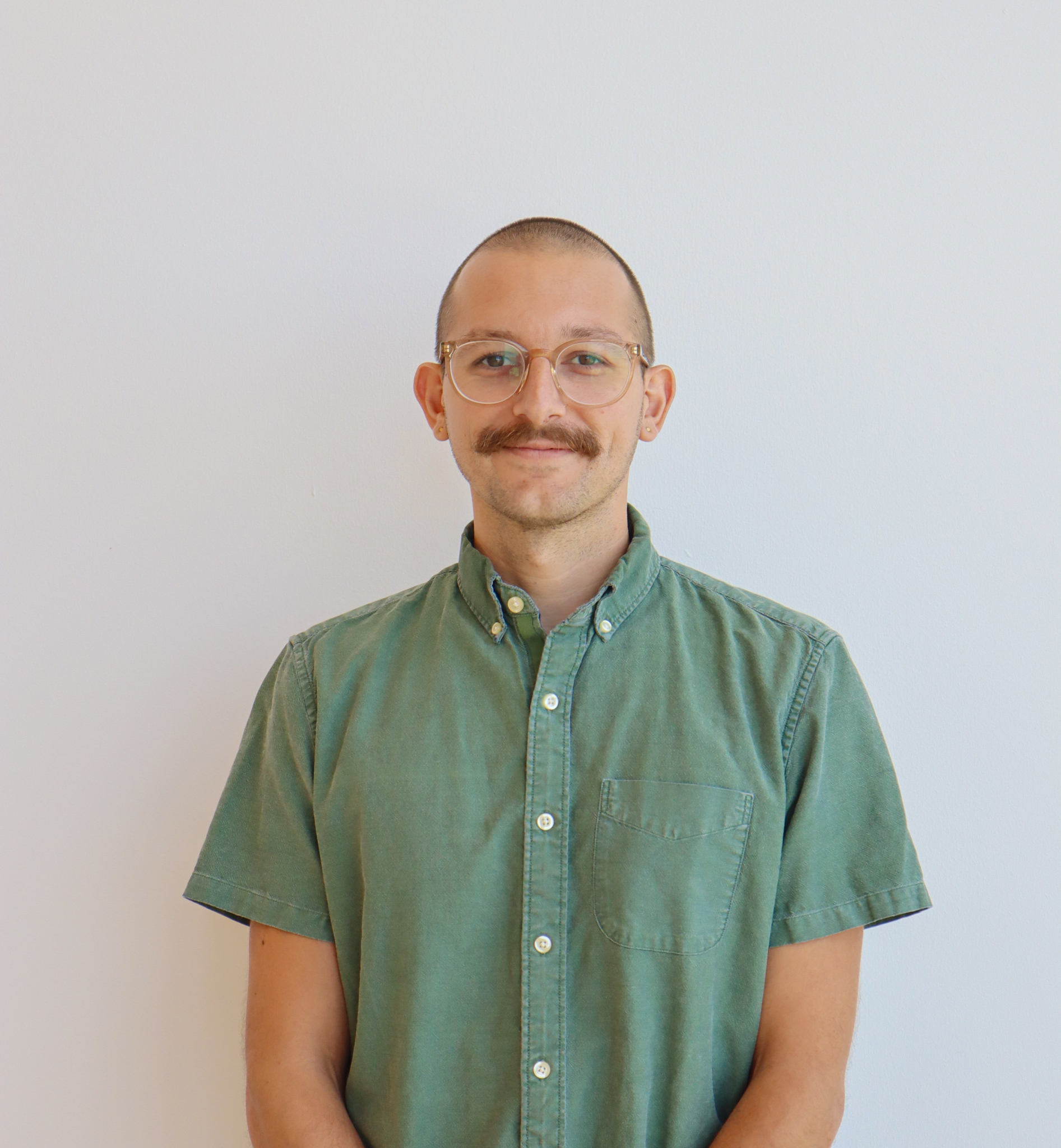A person with a mustache wearing a green button-up shirt and glasses