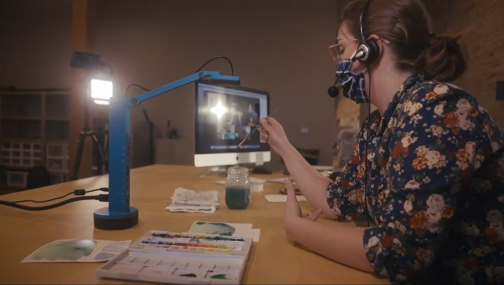 A masked person demonstrates watercolor painting techniques on a video conference call