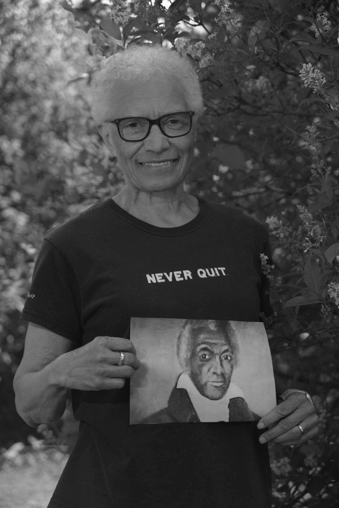 A short-haired woman with glasses holds a portrait of Black man