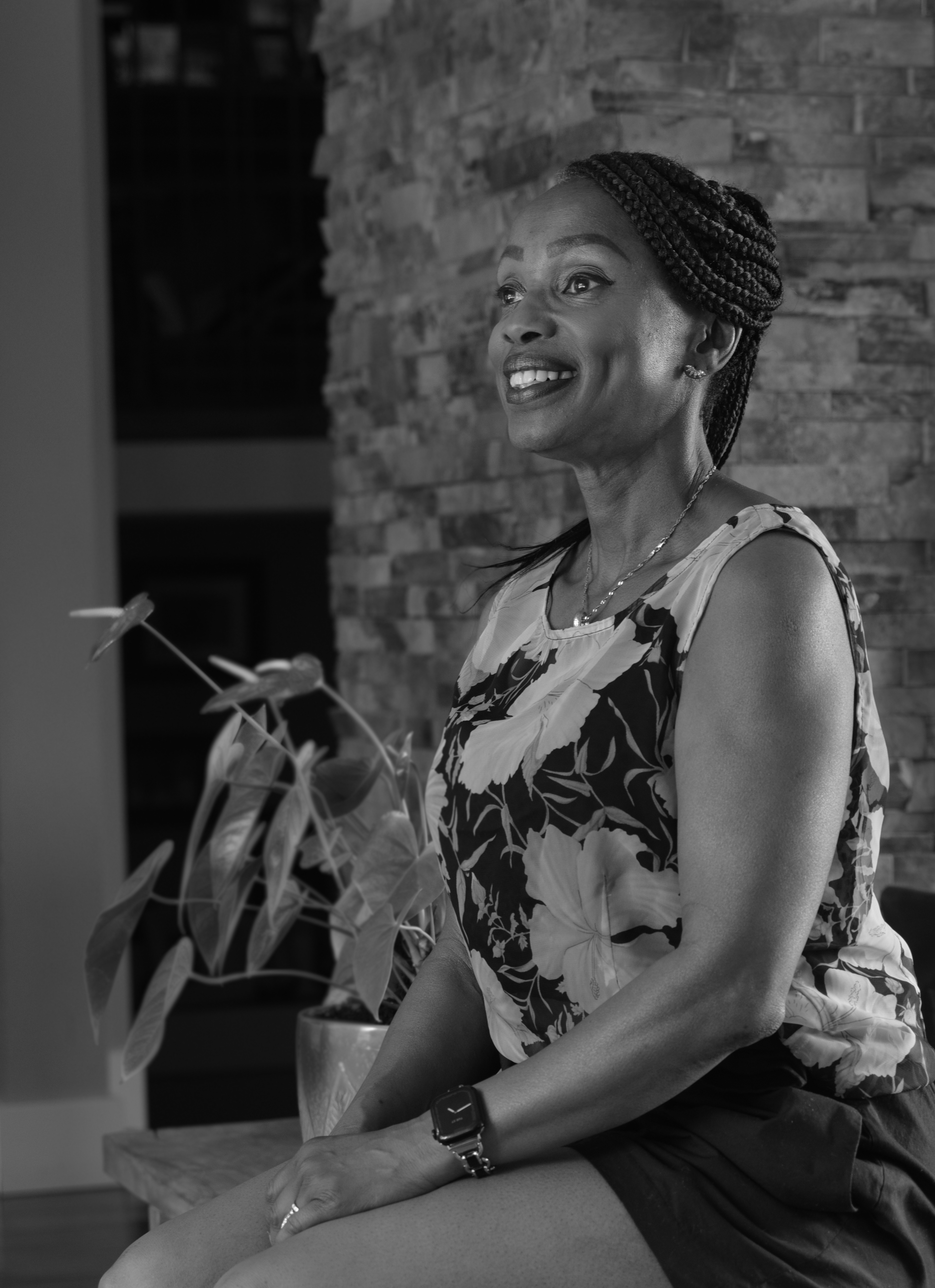 A black-and-white portrait of a Black woman sitting down, from the waist up. The woman is sitting at an angle, smiling widely.