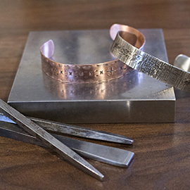 a set of jewelry cuffs rests on a metal block with tools