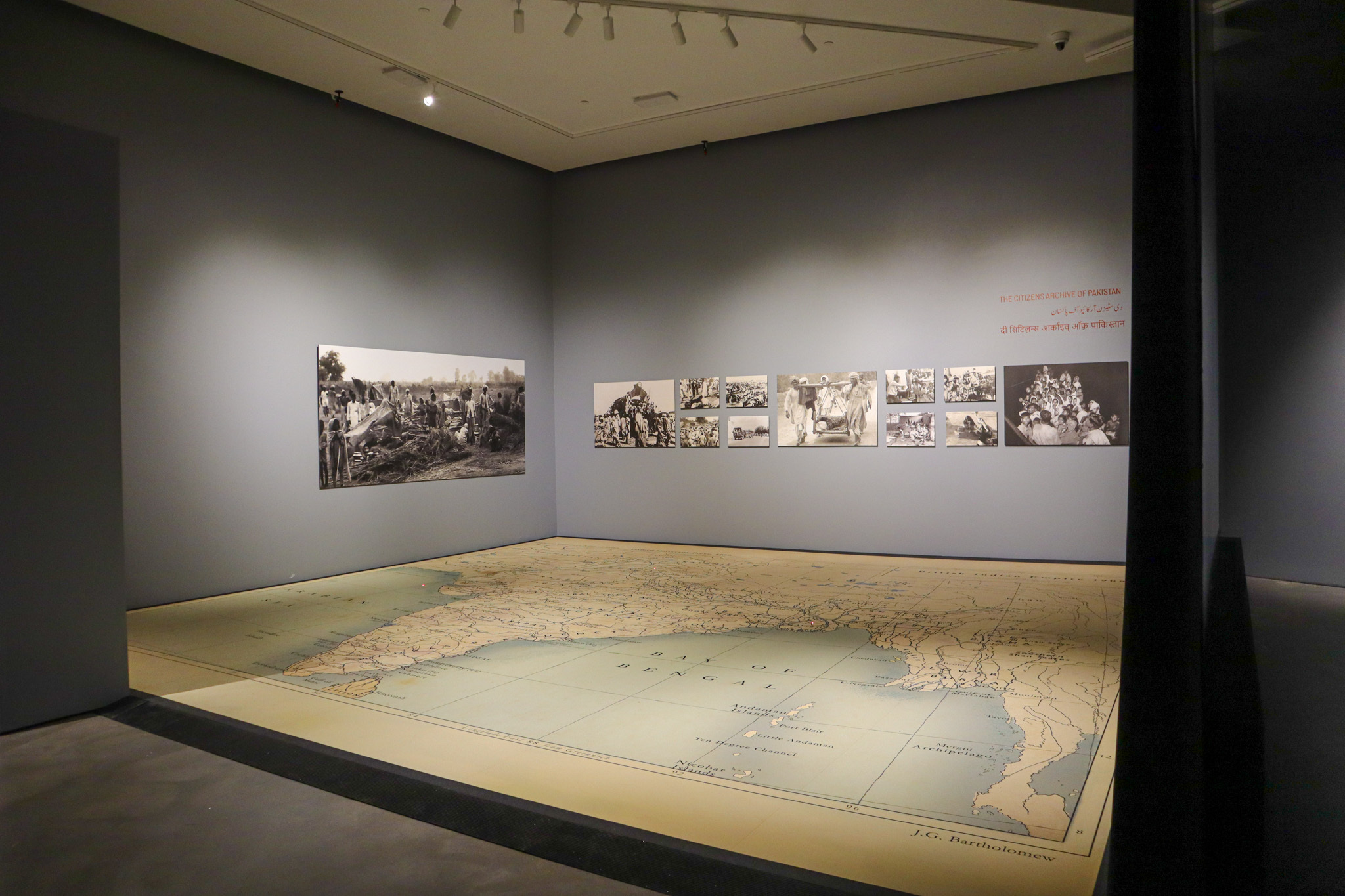 An art gallery with a large interactive map on the ground, and black-and-white rectangular photos lining the wall