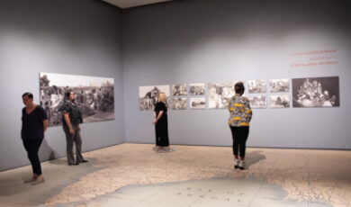 Four people stand on a large map and view black and white photos on the walls
