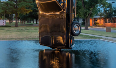 The hood of a black vintage car grazes the surface of a reflecting pool
