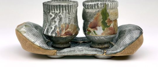 Two ceramic cups patterned with lines and flowers rest on a curved ceramic stand