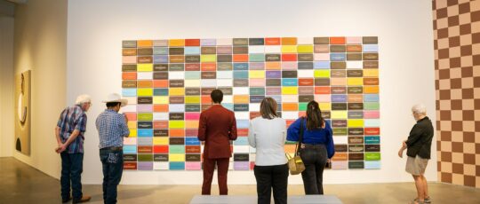 A group of people stand in front of a wall full of colorful tiles