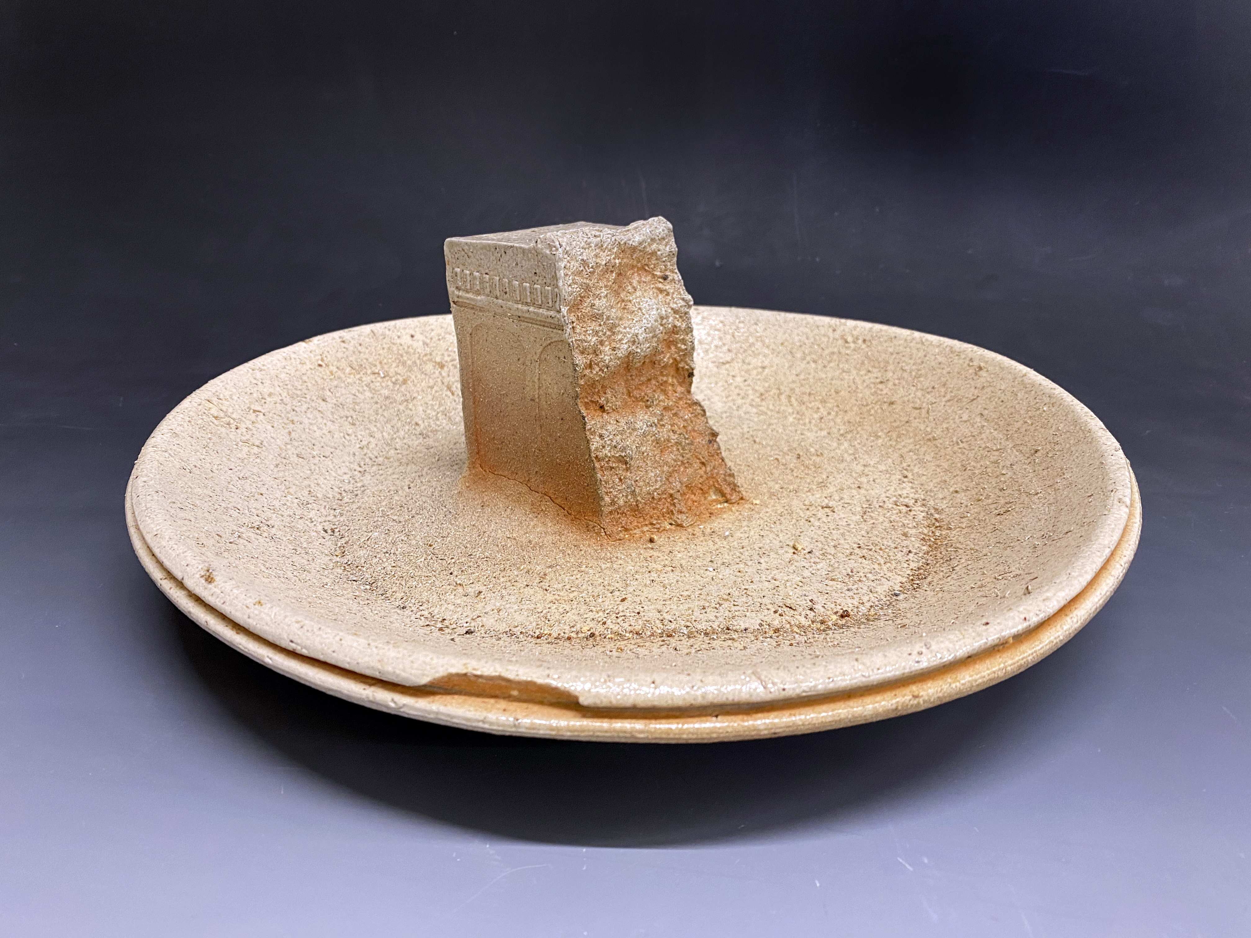 An abstract ceramic sculpture featuring a platter with a protrusion sticking up from the middle