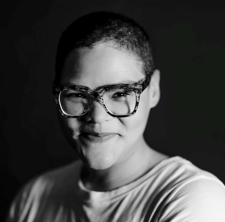 Black and white photo of a person with short hair and glasses smiling at the camera