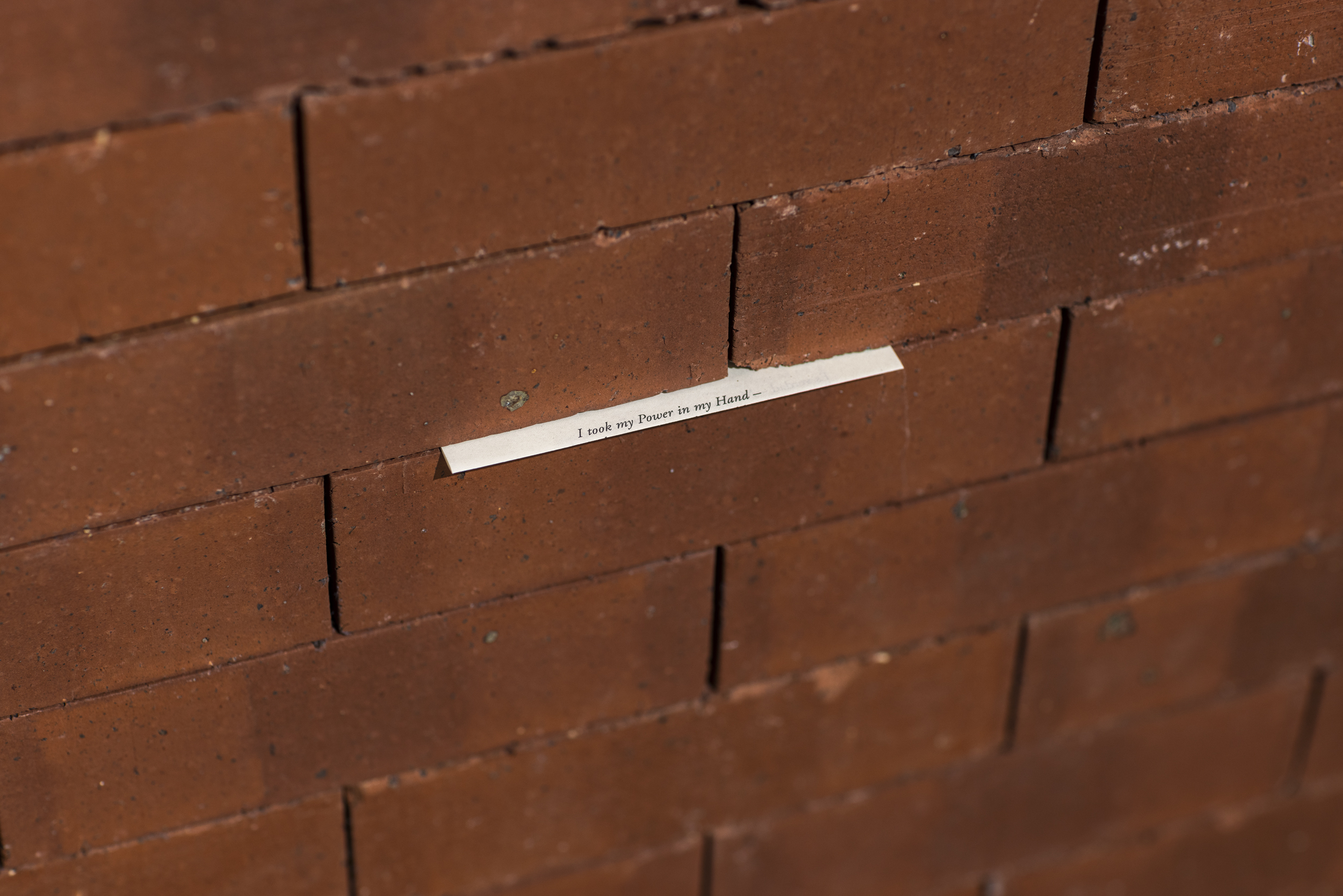 A small slip of paper is sticking out between red bricks. We can see the words "I took my Power in my Hands" typed in small font on the paper.