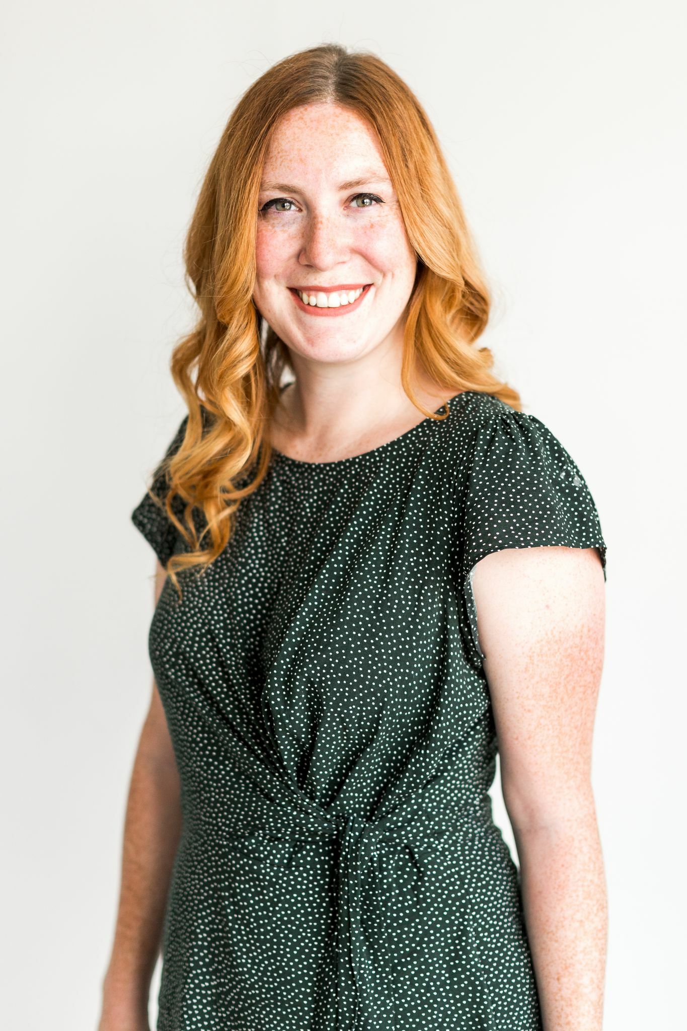 A person with shoulder length red hair wearing a green dress smiles at the camera