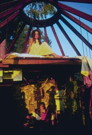 A person with long hair sits on an elevated platform suspended below open beams