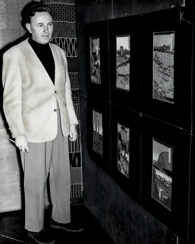 Black and white photo of a man in a suit next to a wall of landscape photos
