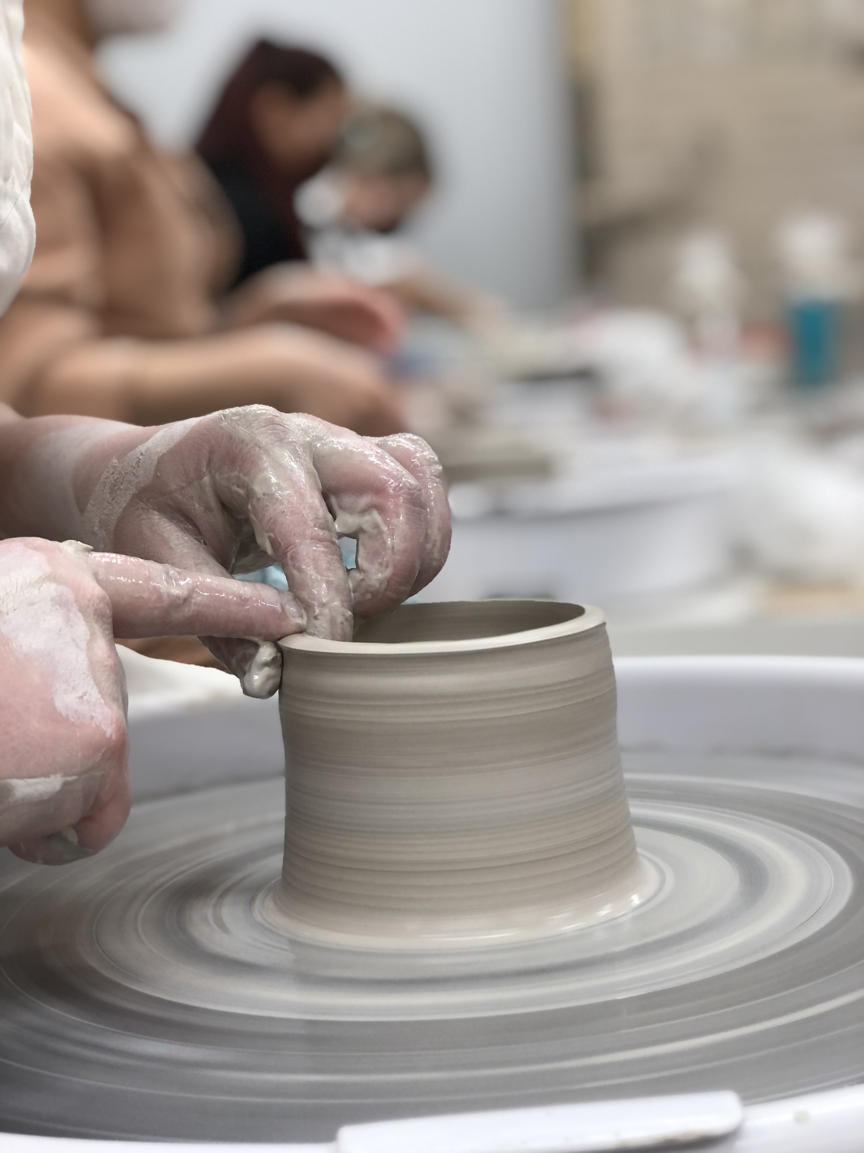 Hands work on the throwing wheel shaping wet clay into a vessel
