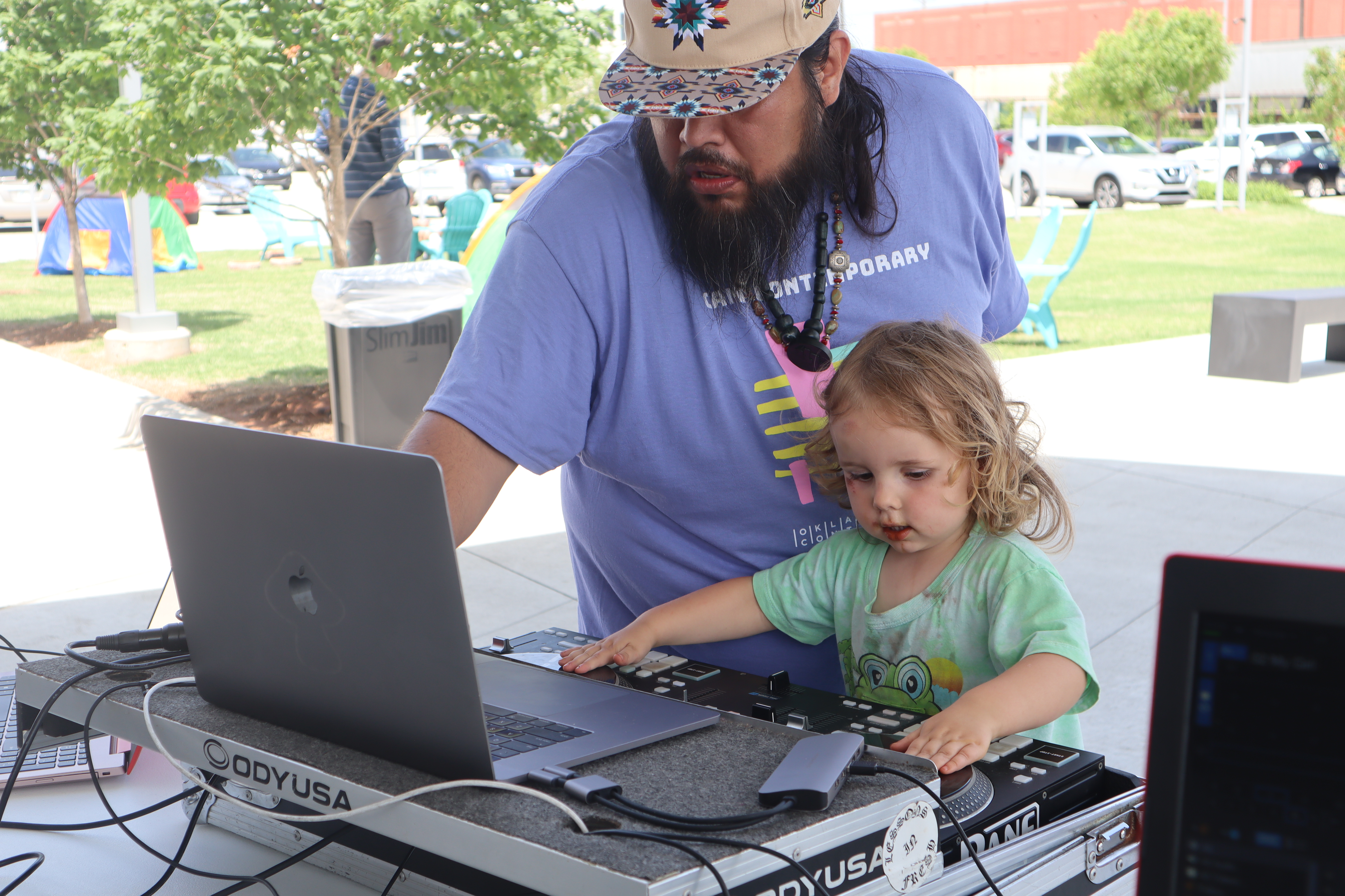 A bearded man in a baseball cap helps a young child operate a turntable
