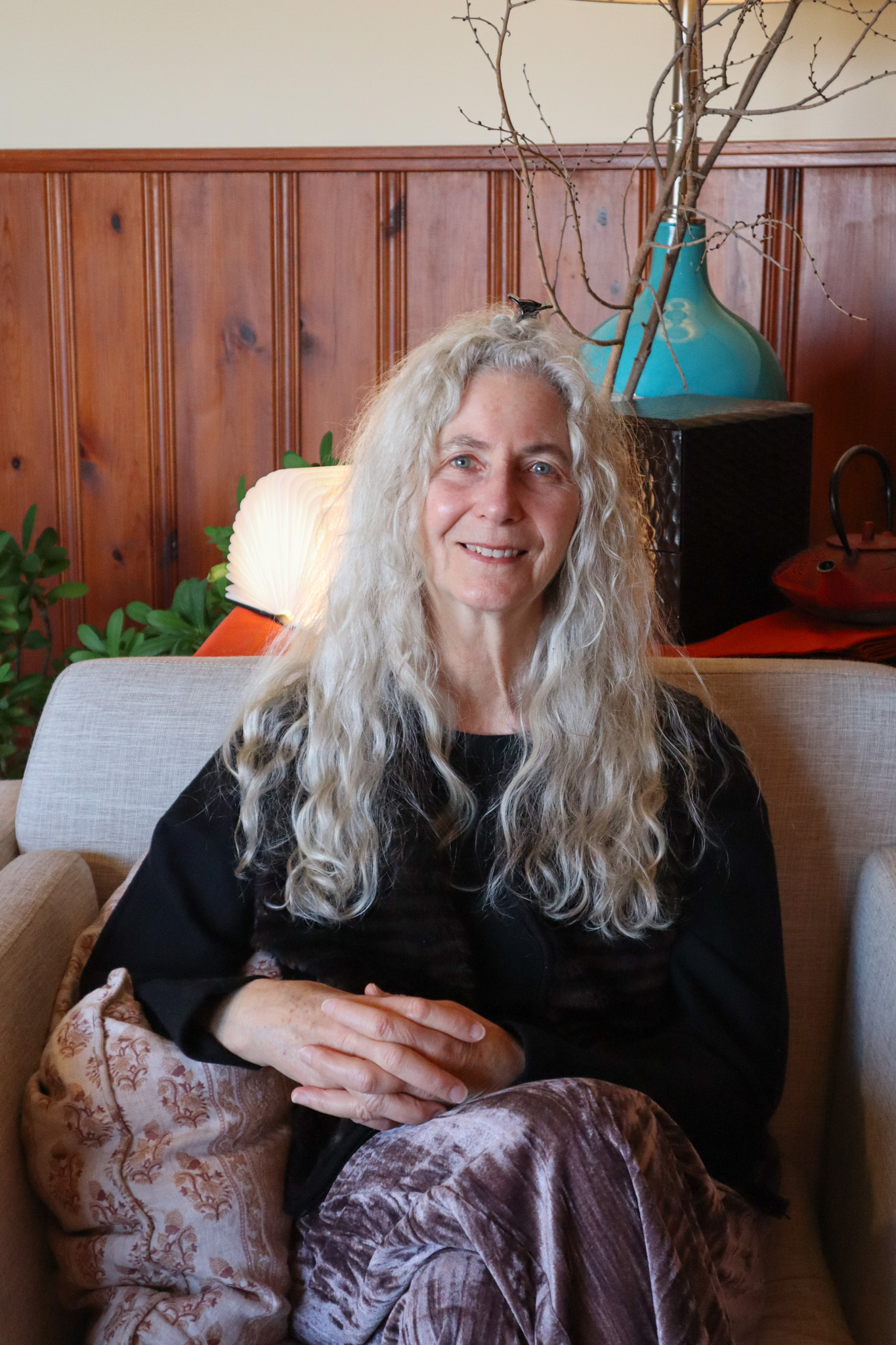 A woman with long, wavy, gray hair sits on a sofa