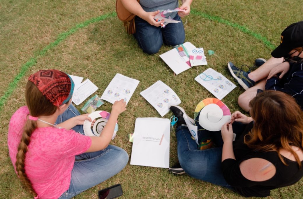 Four people work on hands-on art activities while sitting in the grass