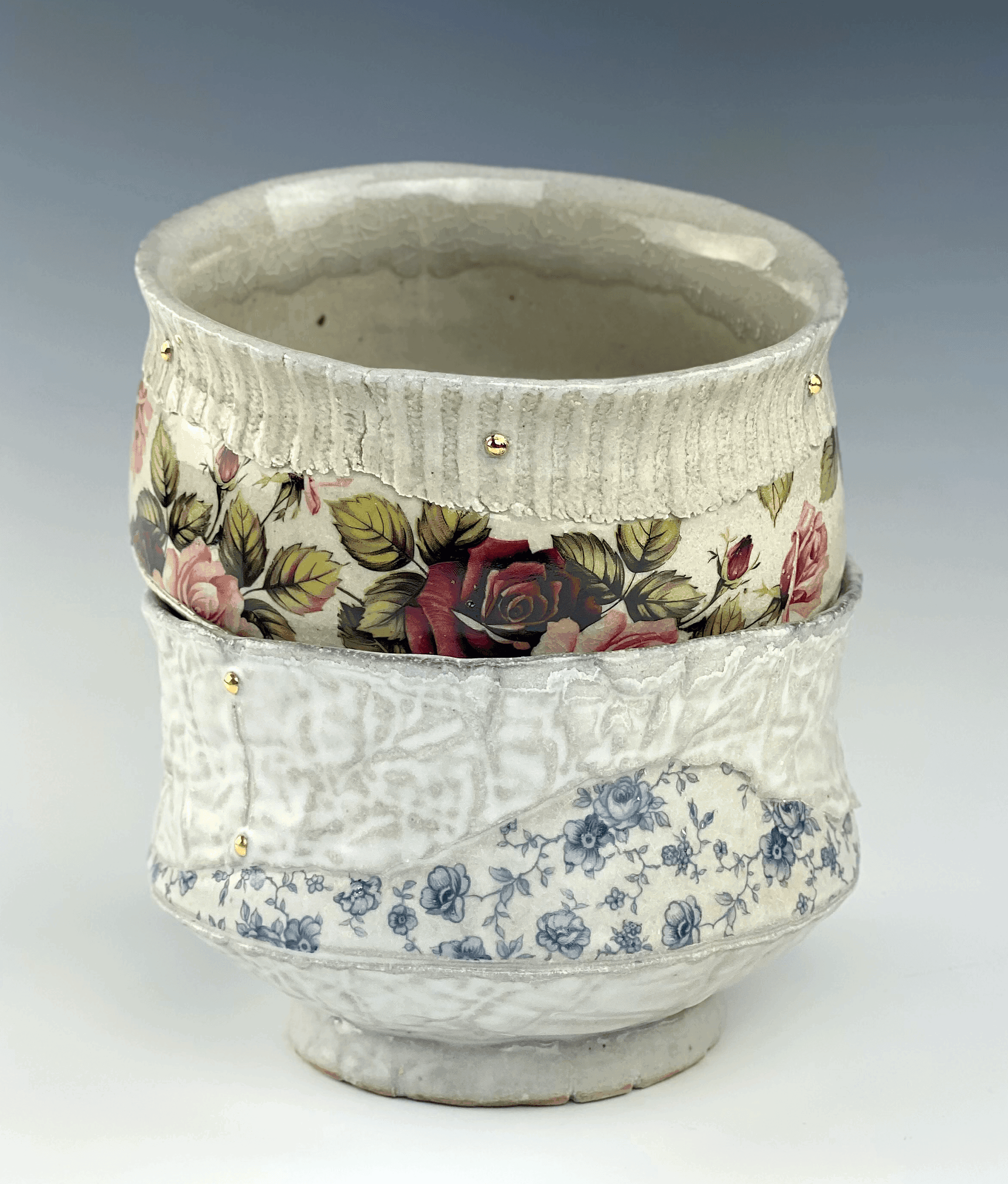 Two ceramic bowls are stacked on top of each other. The bottom bowl has small blue floral details and fiber texture. The top bowl has green and red flower details with a corduroy texture around the rim.