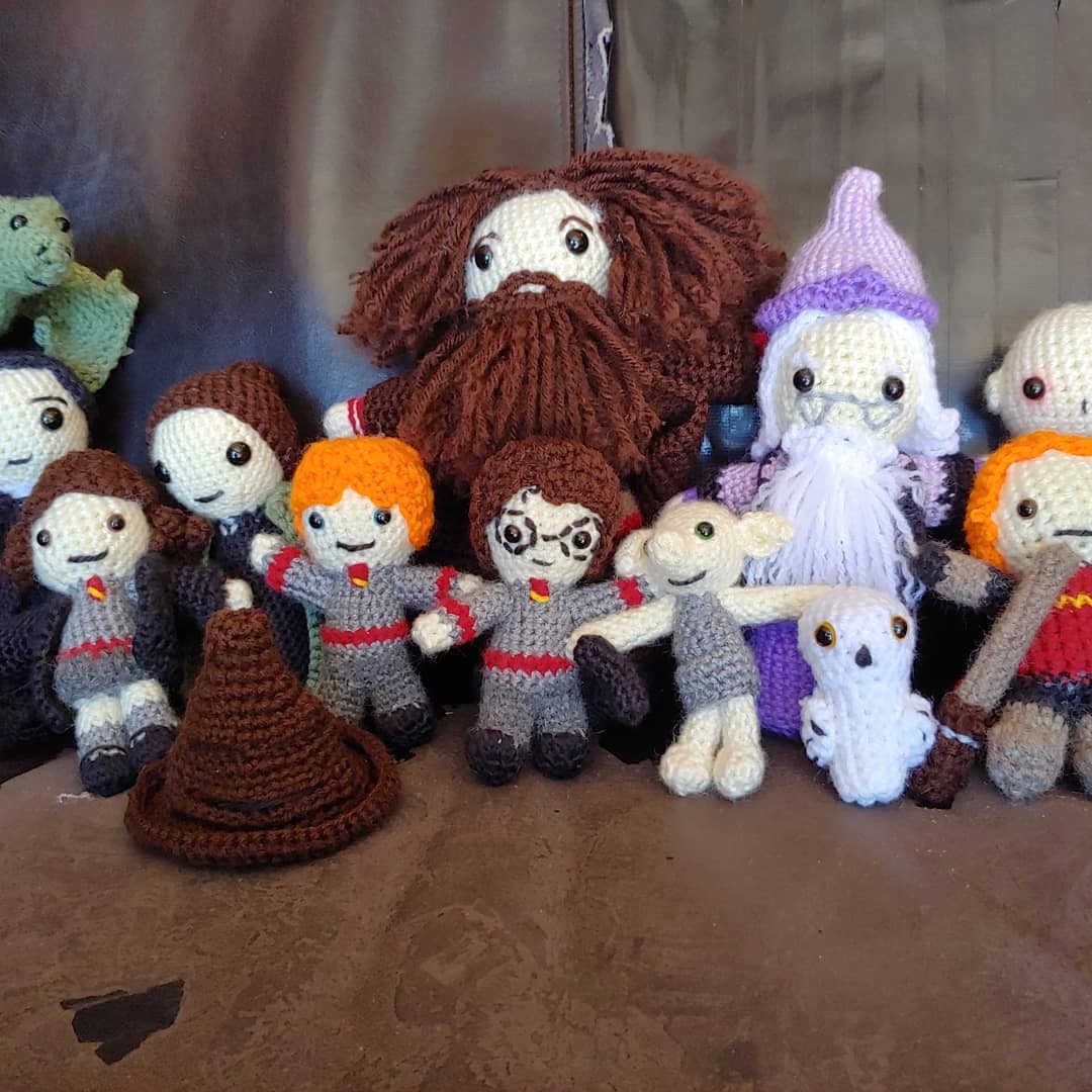 Crocheted Harry Potter characters sit together, including Harry, Ron and Hermione in grey and red uniforms, Dumbledore in a purple robe and hat, and Hagrid with a full beard and hair..