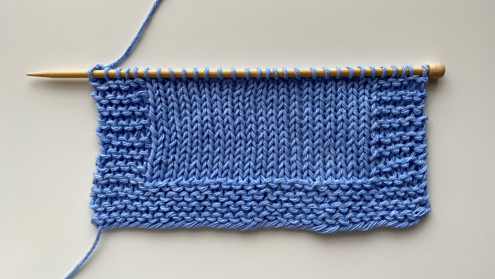 A cropped image of a partially knitted project and a knitting needle wrapped in blue thread