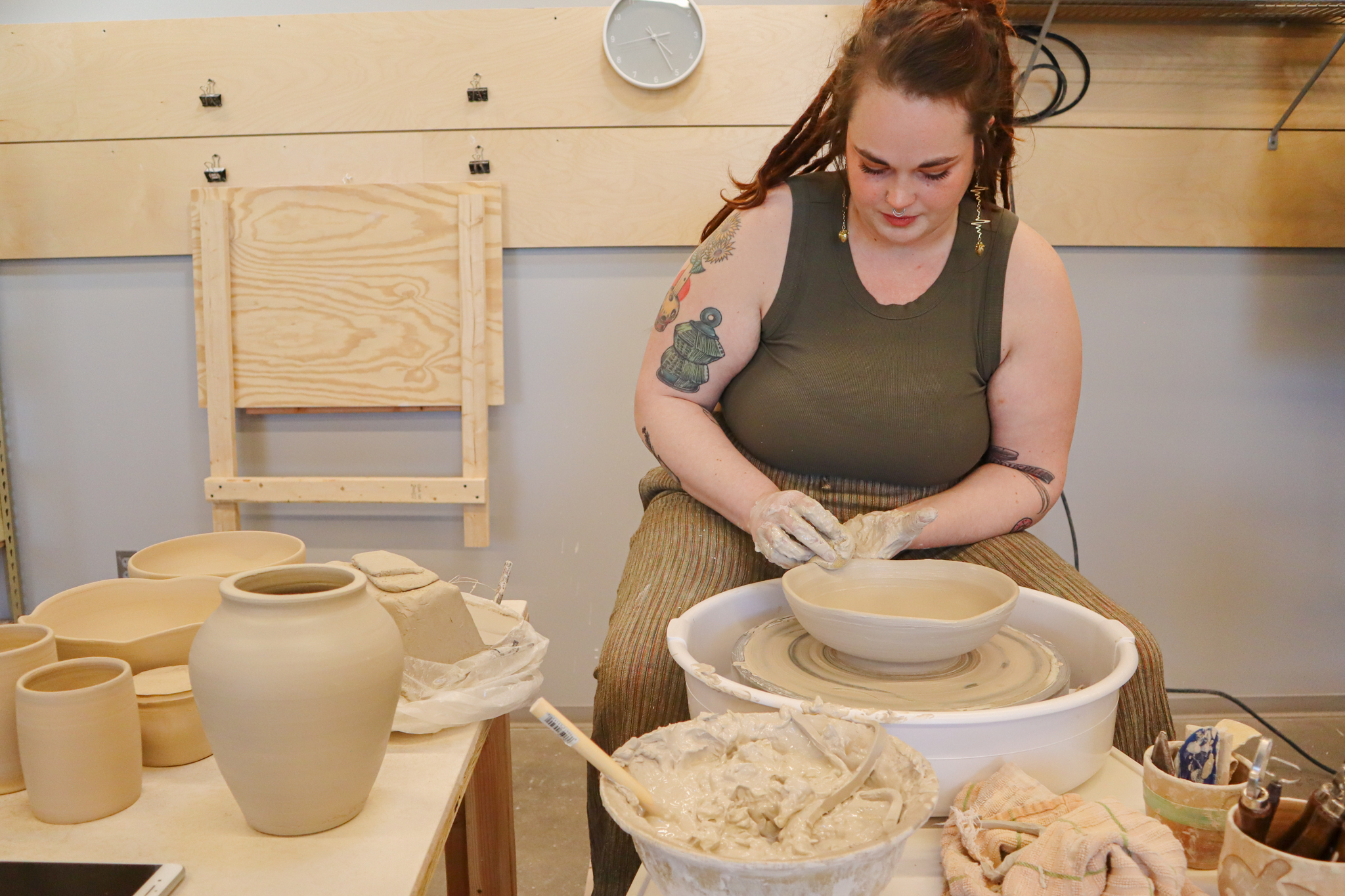 A person is working on a potters wheel surrounded by recently thrown vessels