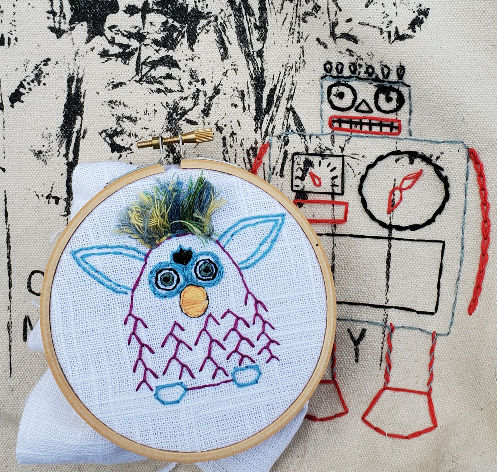 An embroidered furby in blue and pink string with wild hair