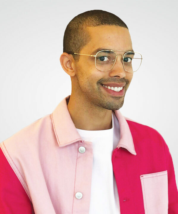 A person with glasses and light and dark pink jacket smiles at the camera