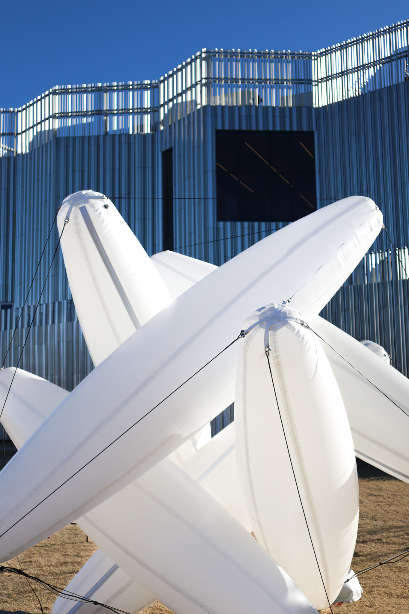 Inflatable white cylindrical forms balanced in front of a silver building