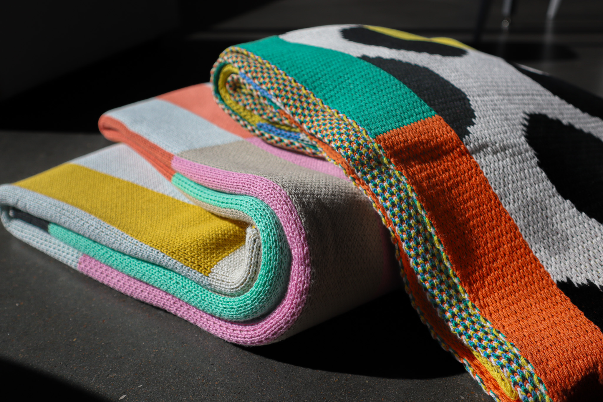 Two colorfully patterned woven blankets are sitting in a stack on a cement floor