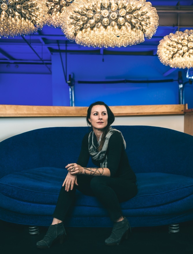 A figure sits on a blue couch beneath three artistic chandeliers