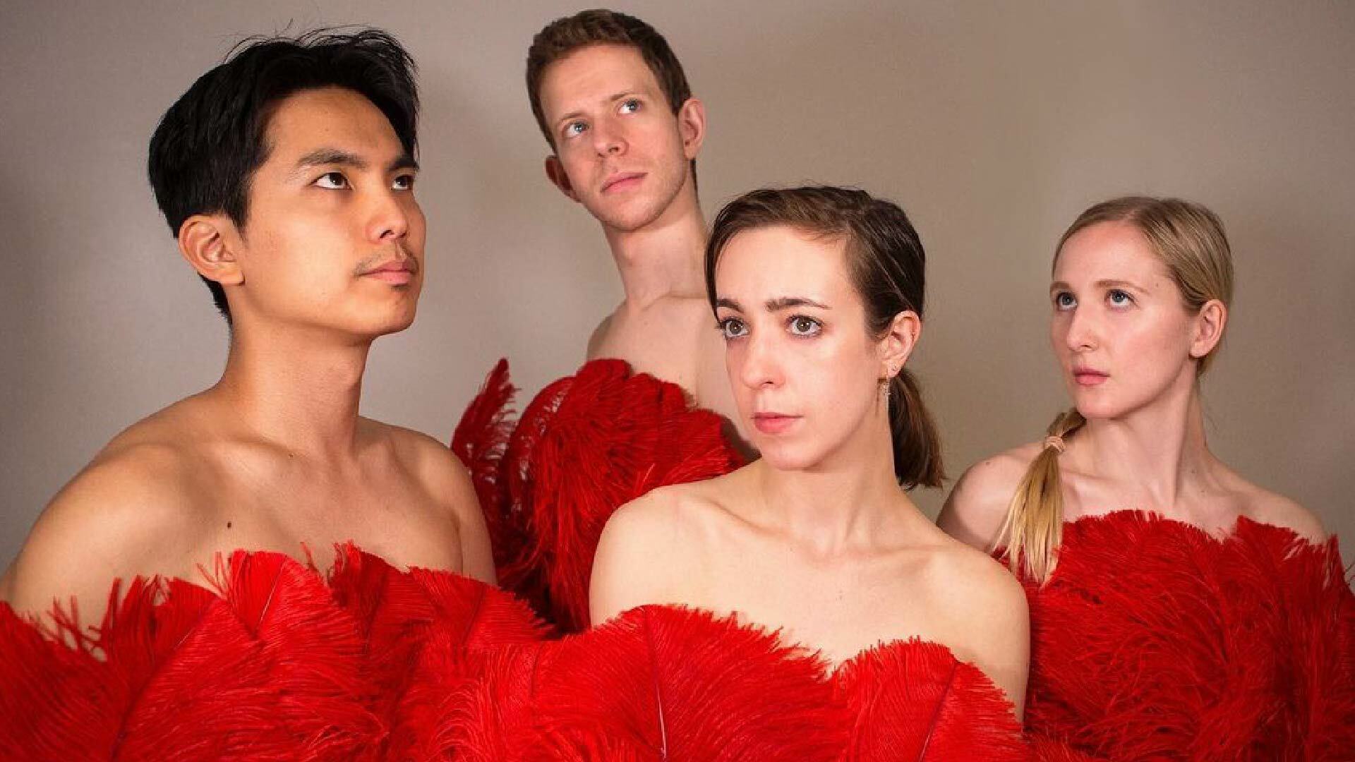 Four people stand together seemingly naked covered by fluffy red feathers from the top of the chest down