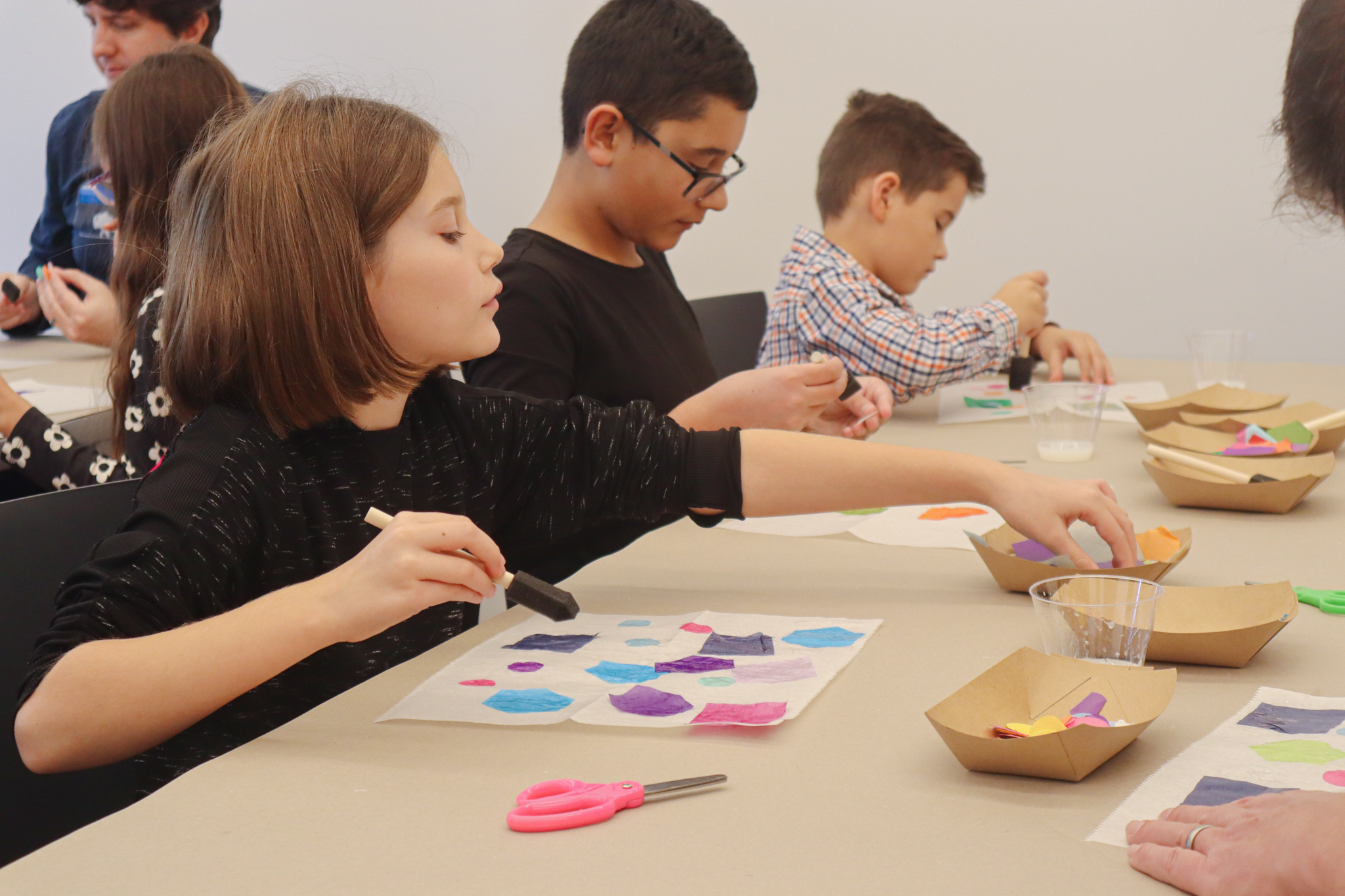 Several children sit at a table engaged in art making