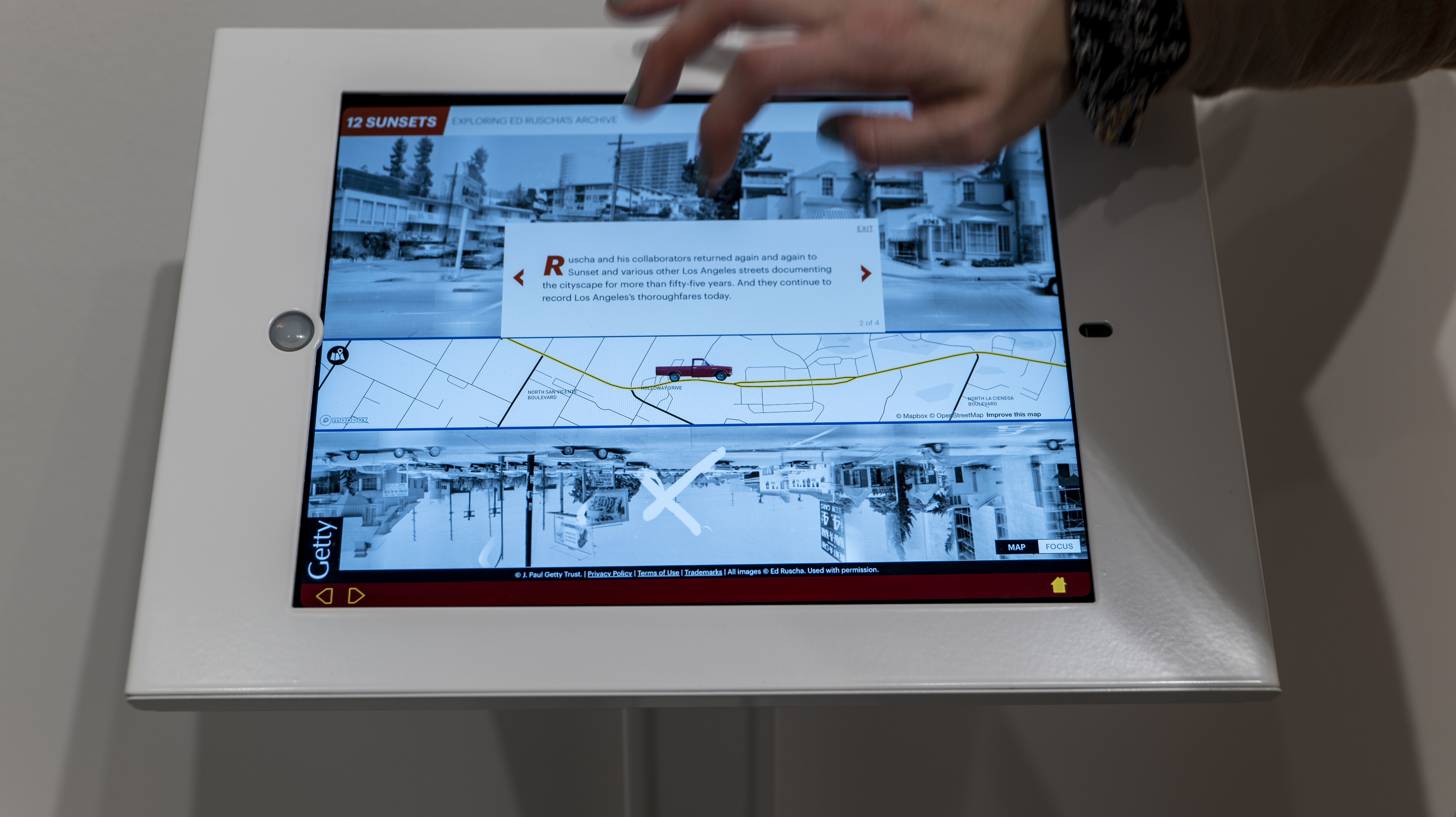 A hand manipulates an iPad touch screen depicting images of a street dense with cars and buildings