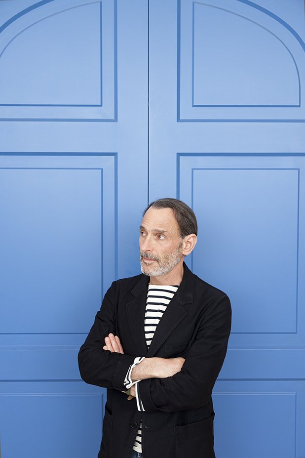 David Salle, a man in a striped shirt and black blazer, poses against a blue door