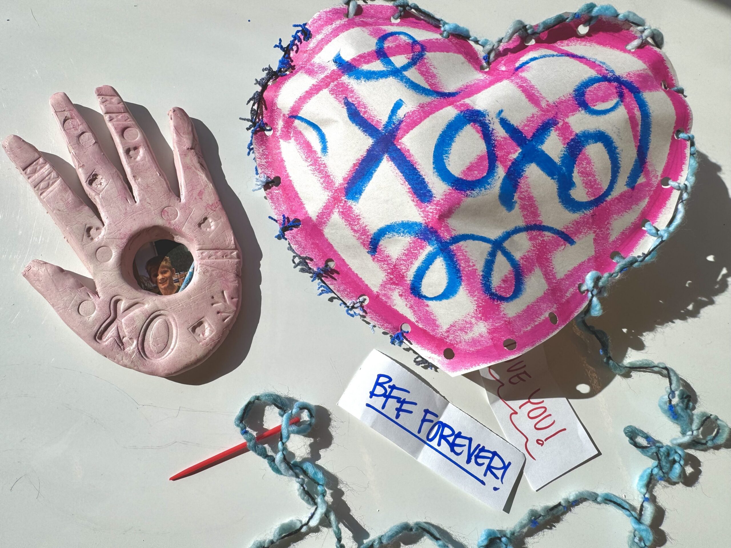 Art projects, including a clay handprint and paper heart, lay on a table