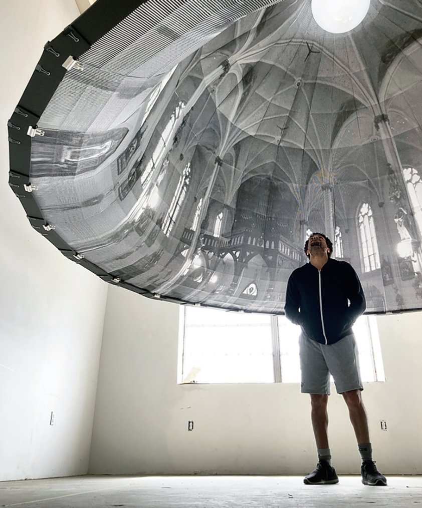 A Black man stands under a dome printed with an image of the inside of a church