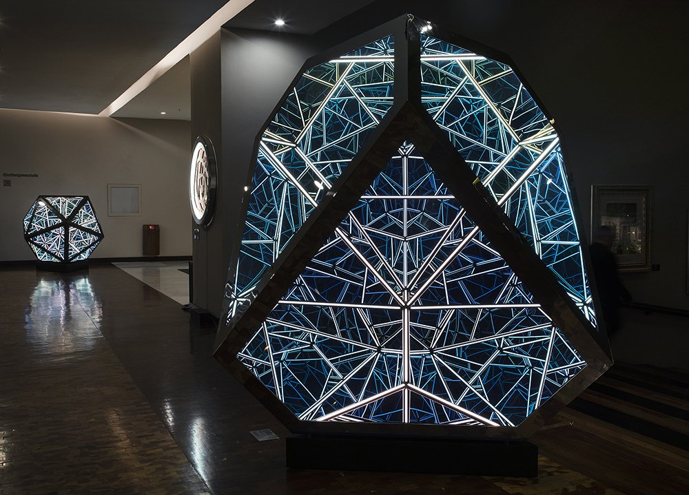 Two geometric sculptures with internal lights reflecting in geometric patterns