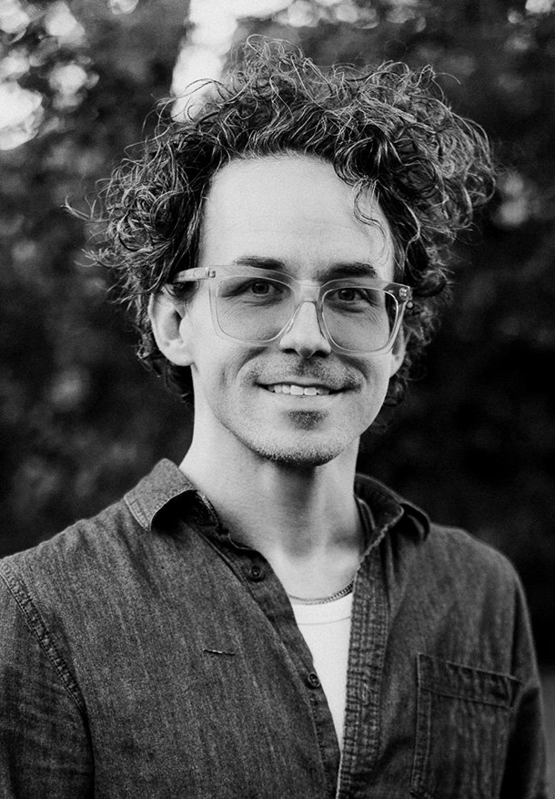 A black and white photo of Blake Studdard, a man with curly hair and glasses
