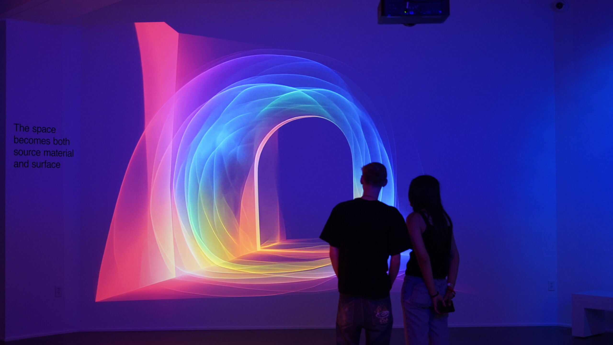 Two people stand in front of a brightly colored light projection
