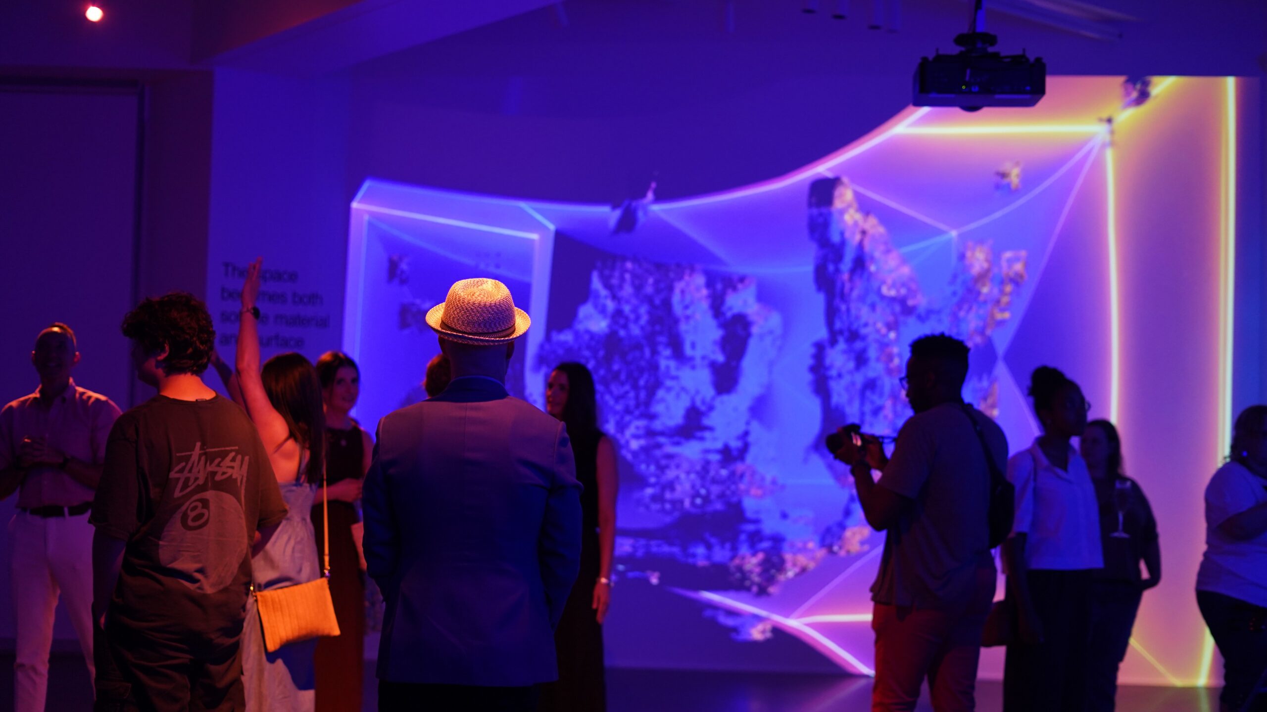 People stand in a gallery full of light projections