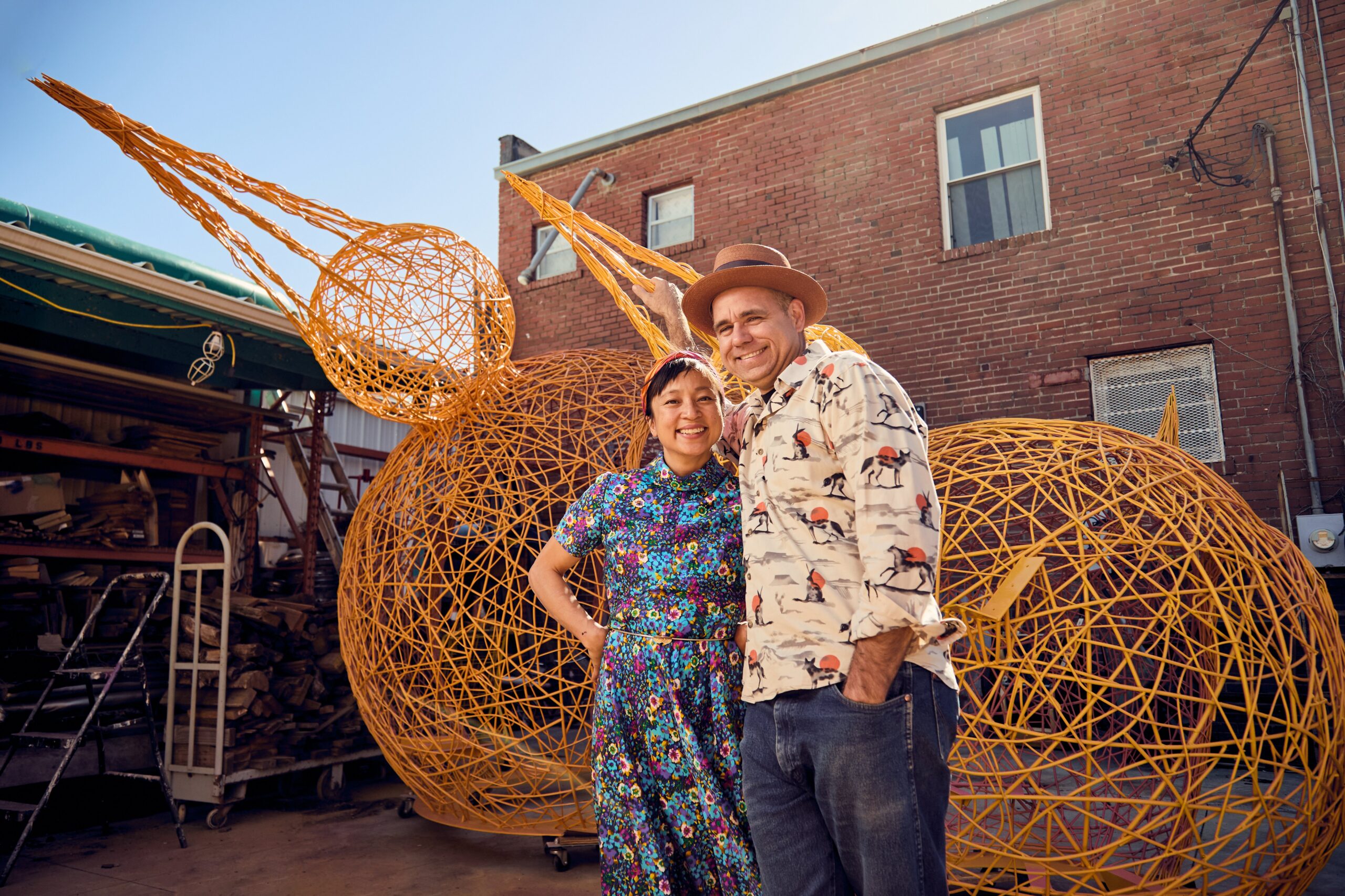 Denise Duong and Gabriel Friedman stand in front of a yellow, birdlike sculpture