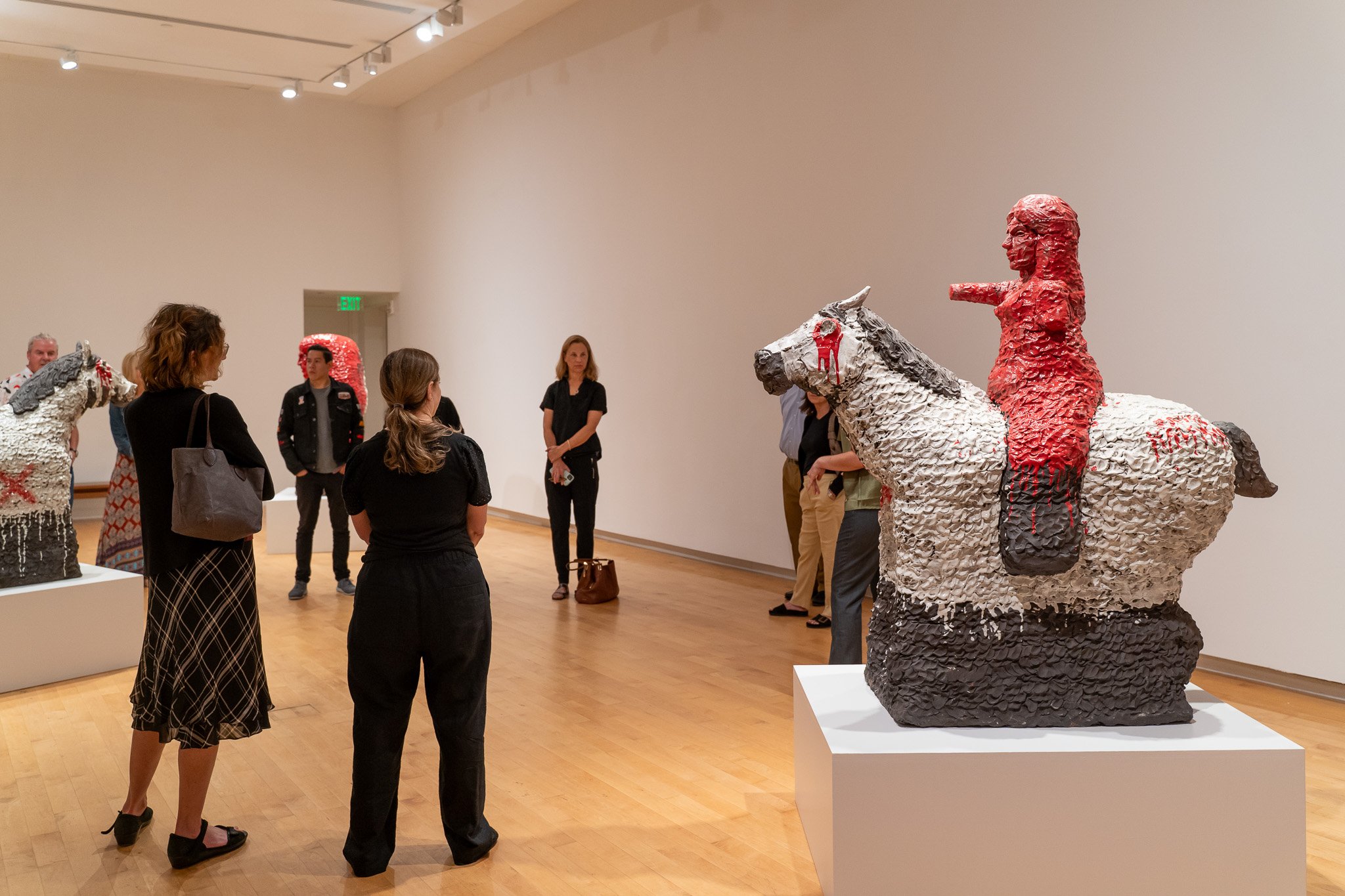 A group of people stand around a large ceramic sculpture of a woman on a horse