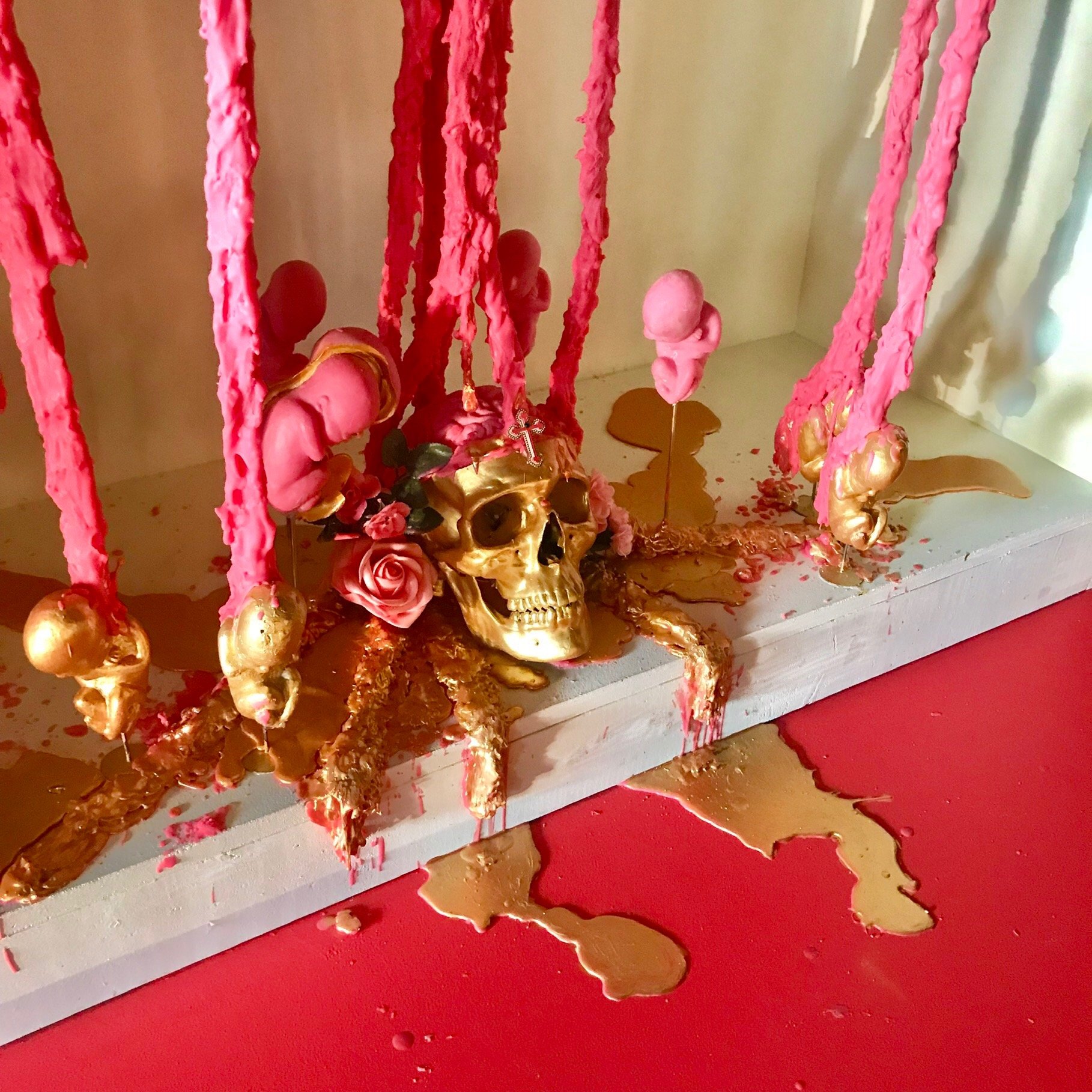 A gold skull surrounded by gold and pink babies and melted wax