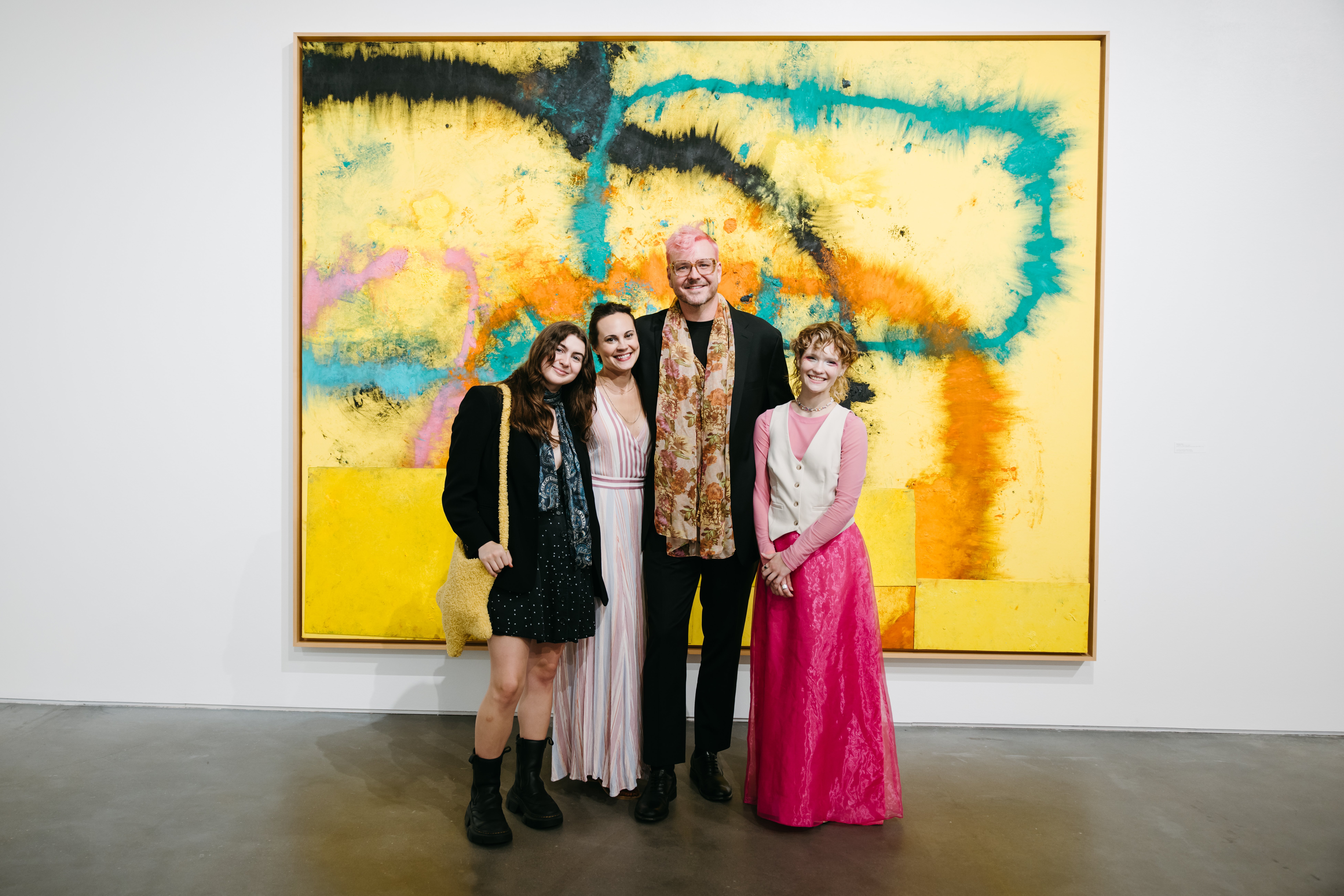 Four people smile in front of painting in gallery