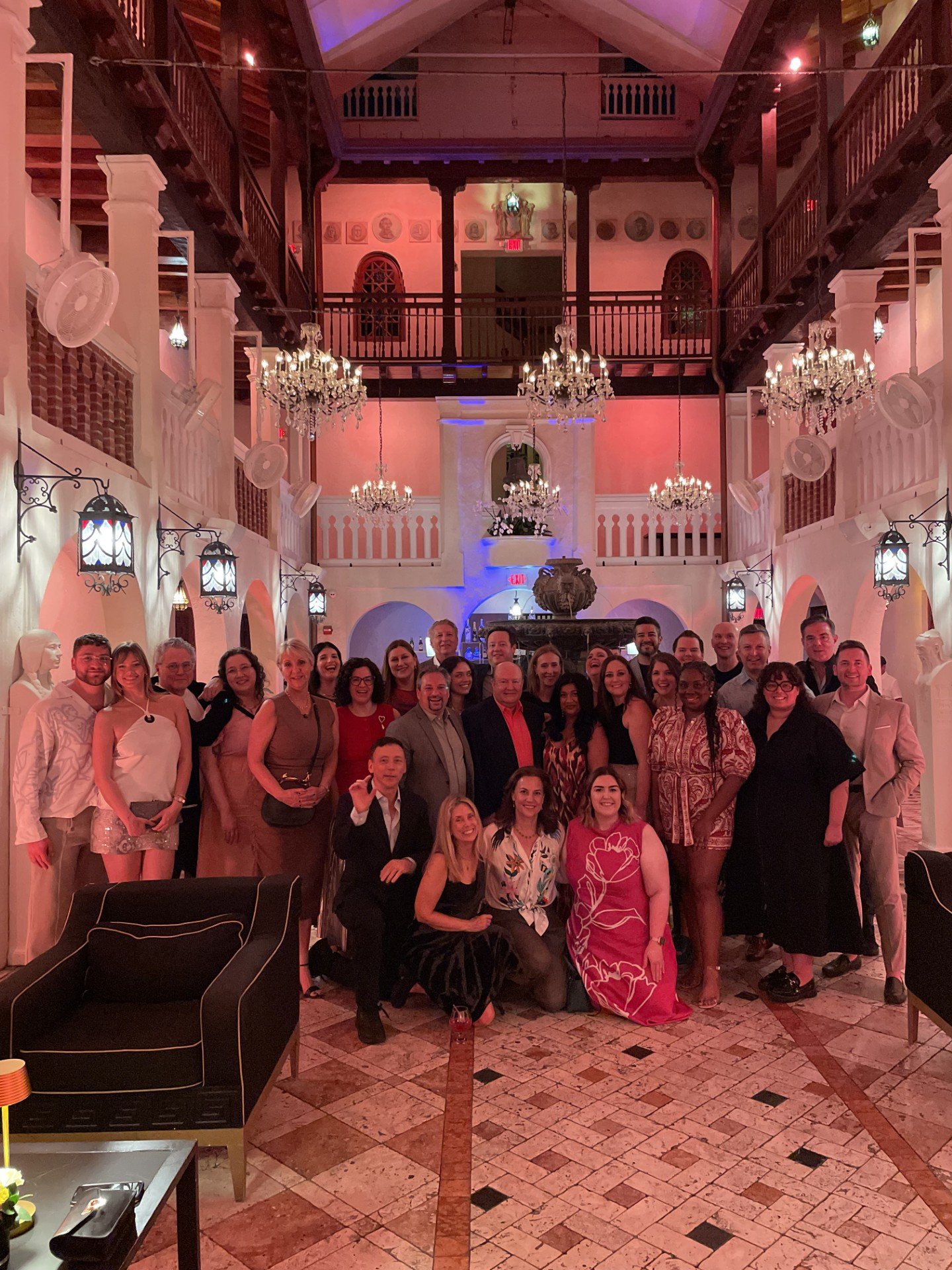 A group of people pose in a titled lobby with hanging chandeliers