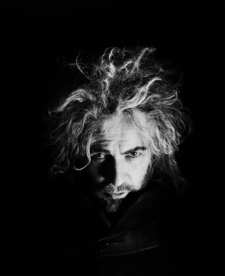 Dramatic black and white photo of Wayne Coyne, a man with a beard and unruly hair