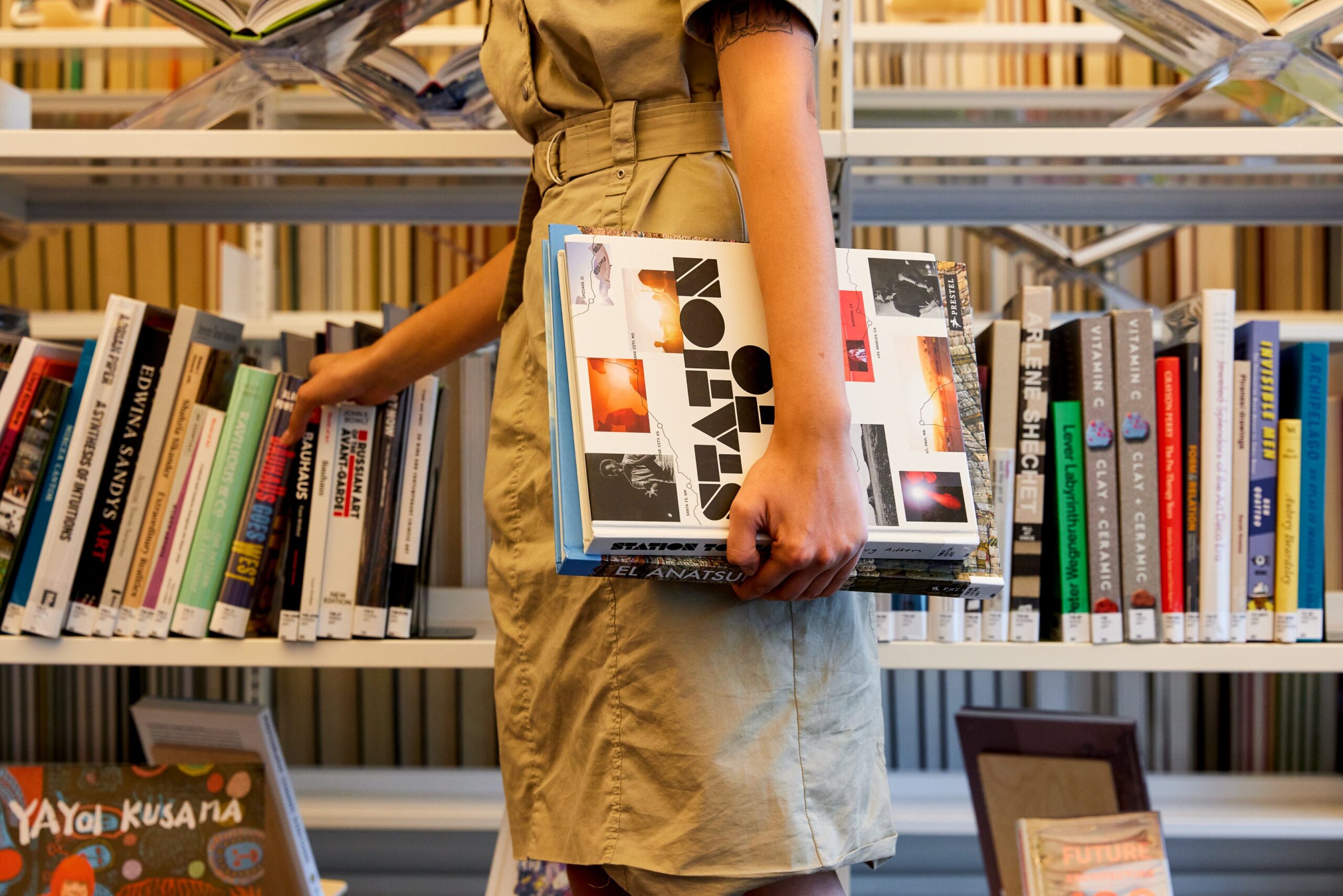 A person holding books walks along a bookshelf